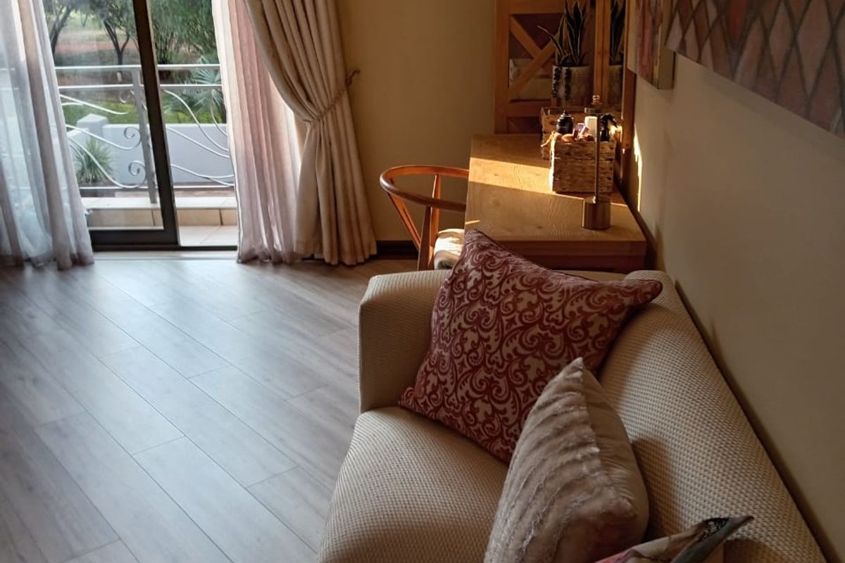 A comfortable living room featuring light-toned laminate flooring, a wall-mounted air conditioning unit, and a sliding glass door leading to an outdoor balcony.