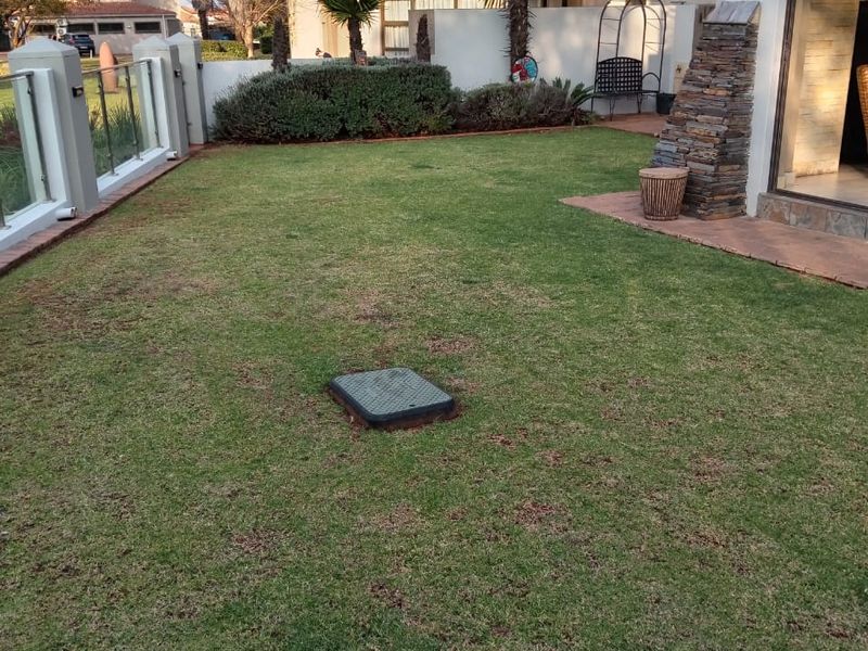 A private rear garden featuring a manicured lawn, glass balustrade fencing, and a decorative stone-clad pillar adjacent to the patio entrance.