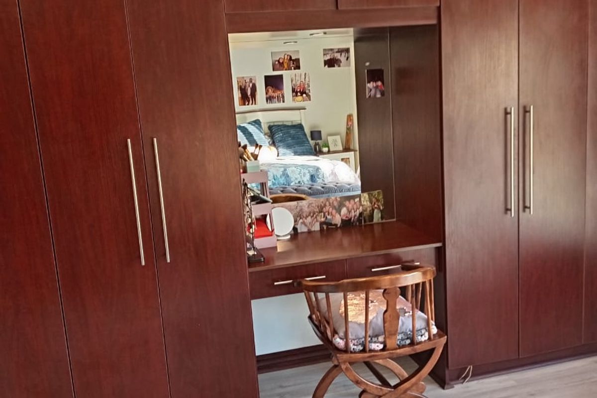 A bedroom featuring extensive dark wood built-in cupboards with an integrated vanity station and modern light-toned laminate flooring.