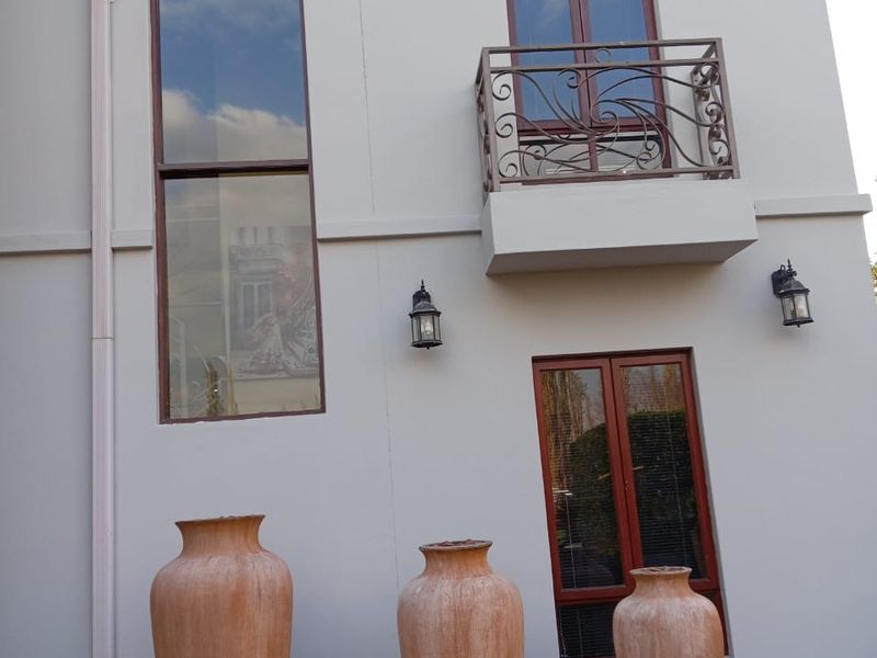 A view of the rear exterior facade featuring a small balcony with wrought iron railing, casement windows, and decorative wall lighting.