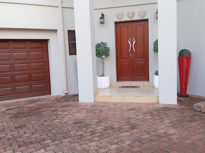 Front elevation featuring a paved driveway, double garage, and a covered entrance porch with double wooden doors.
