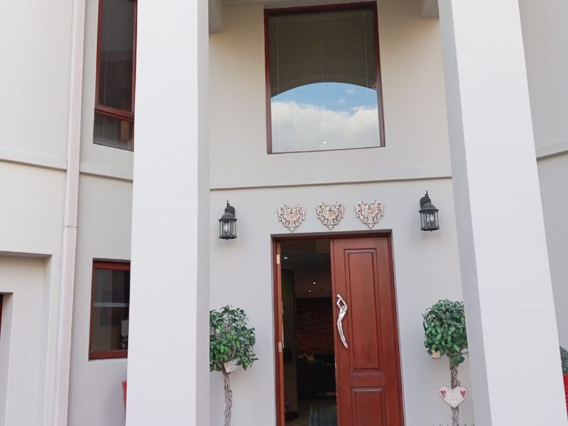 A well-maintained double-storey front entrance featuring large structural pillars, a solid wooden front door, and a tiled porch area.