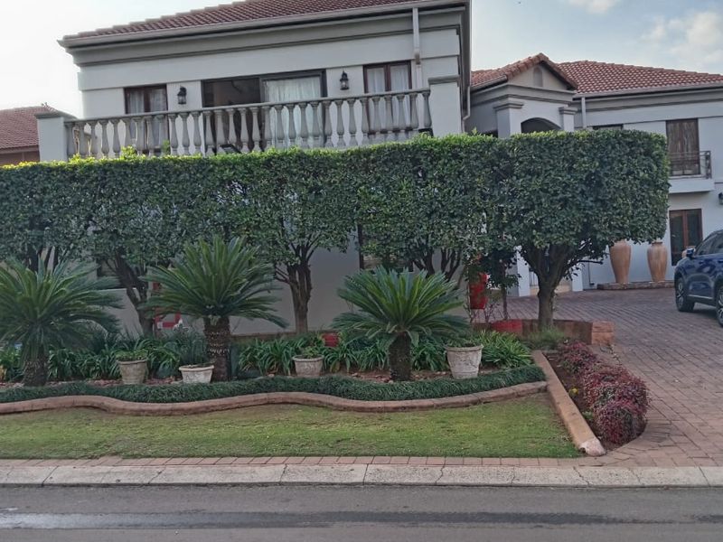 Front elevation of a two-story house featuring a paved driveway, manicured garden, and an upper-level balcony with a classic balustrade.