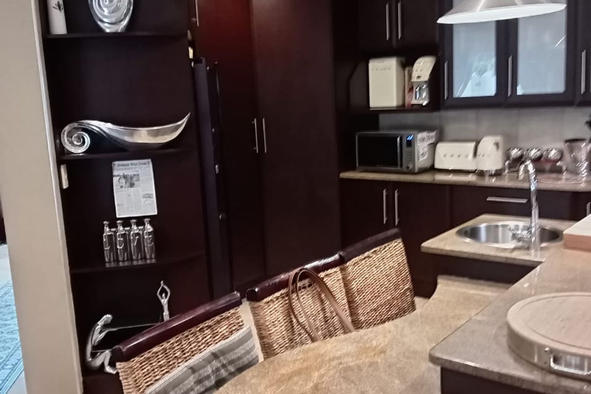 A functional kitchen featuring dark wood cabinetry, granite countertops, an undermount sink, and integrated shelving, illuminated by pendant and recessed lighting.