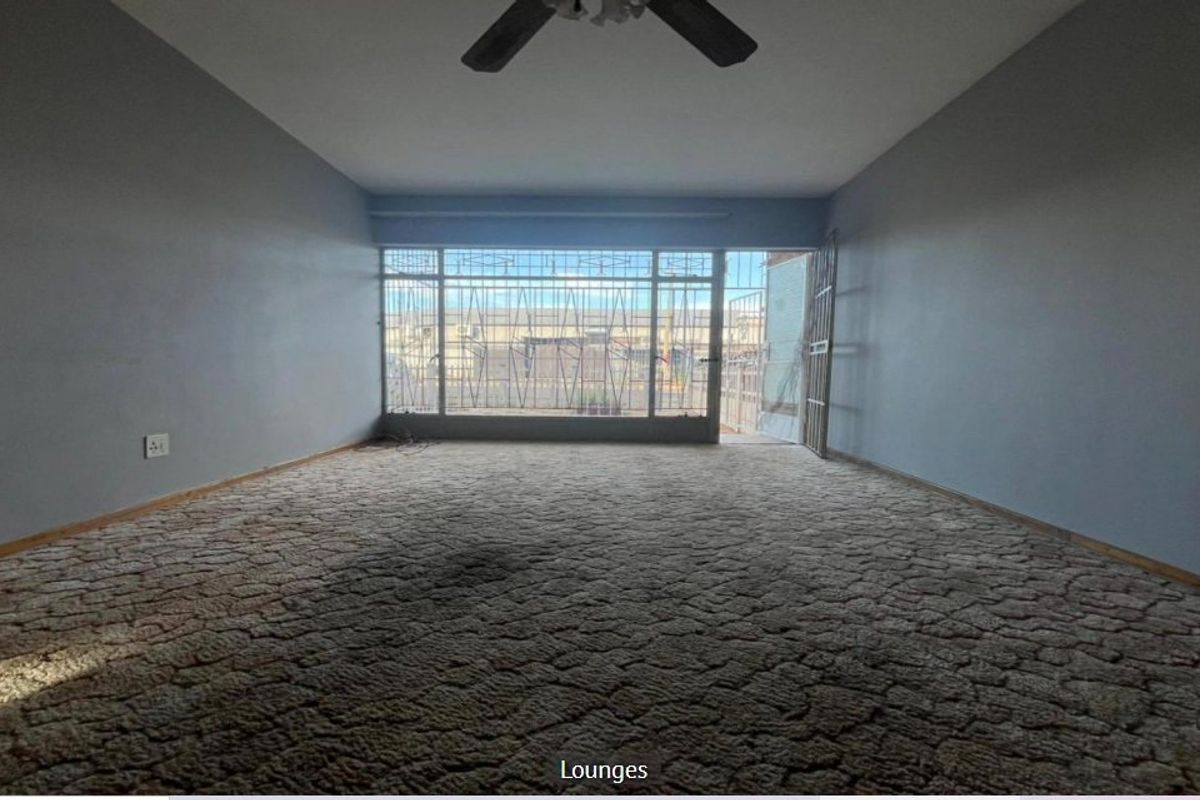An empty living room featuring a ceiling fan, carpeted flooring, and large windows with security bars leading to an outdoor area.