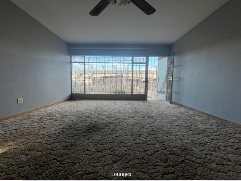 An empty living room featuring a ceiling fan, carpeted flooring, and large windows with security bars leading to an outdoor area.