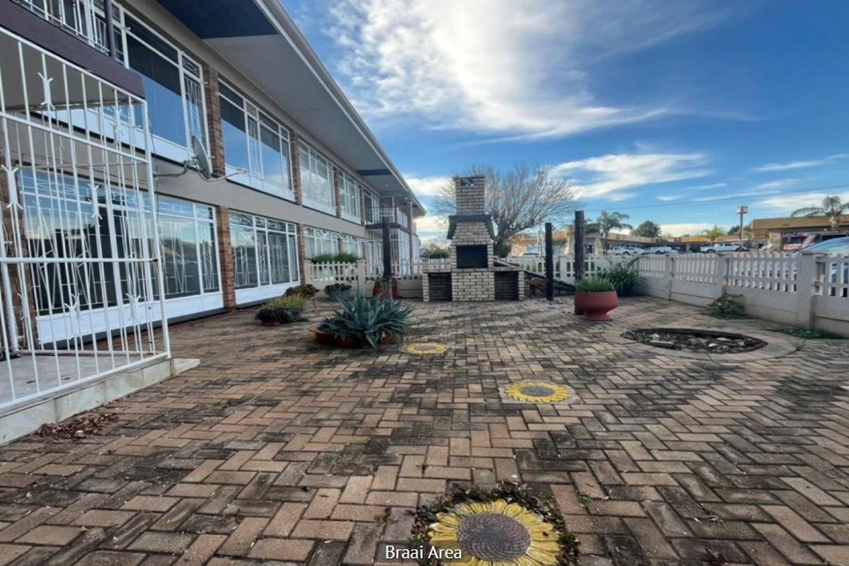 A paved outdoor communal area featuring a built-in brick braai and perimeter fencing, situated at the rear of the apartment complex.