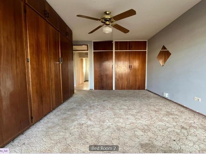 Spacious bedroom featuring extensive built-in wooden cupboards, a ceiling fan, and neutral carpeting, offering a blank canvas for modernization.