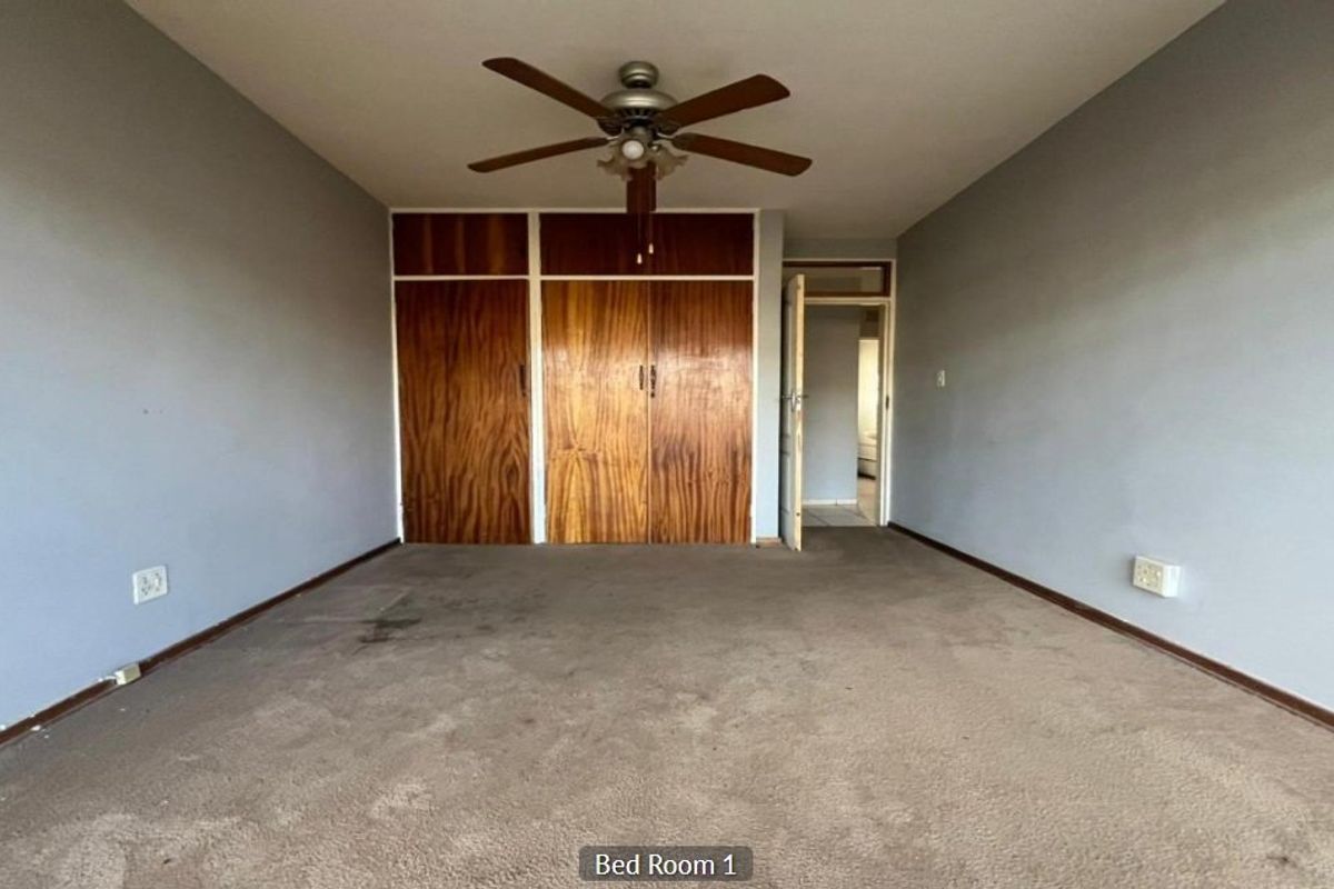 An empty bedroom featuring built-in wooden cupboards, a ceiling fan, and carpeted flooring, offering a blank canvas for renovation.