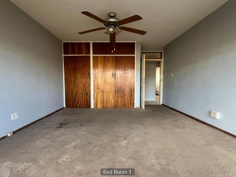 An empty bedroom featuring built-in wooden cupboards, a ceiling fan, and carpeted flooring, offering a blank canvas for renovation.