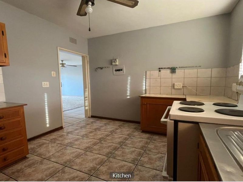 A functional kitchen featuring tiled flooring, wooden cabinetry, and an electric stove, offering a blank canvas for potential modern updates.