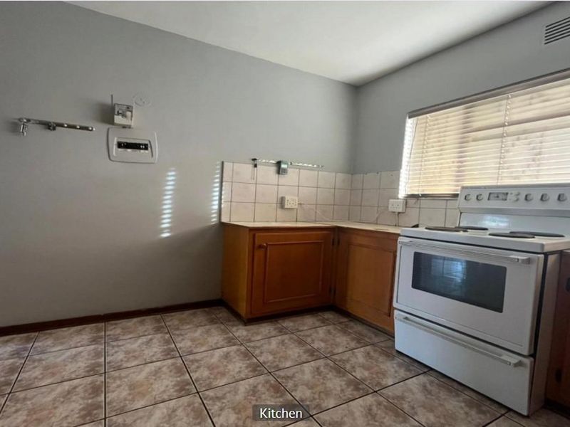A functional kitchen featuring wooden cabinetry, tiled backsplash, and tiled flooring, offering a blank canvas for potential modern updates and renovation.