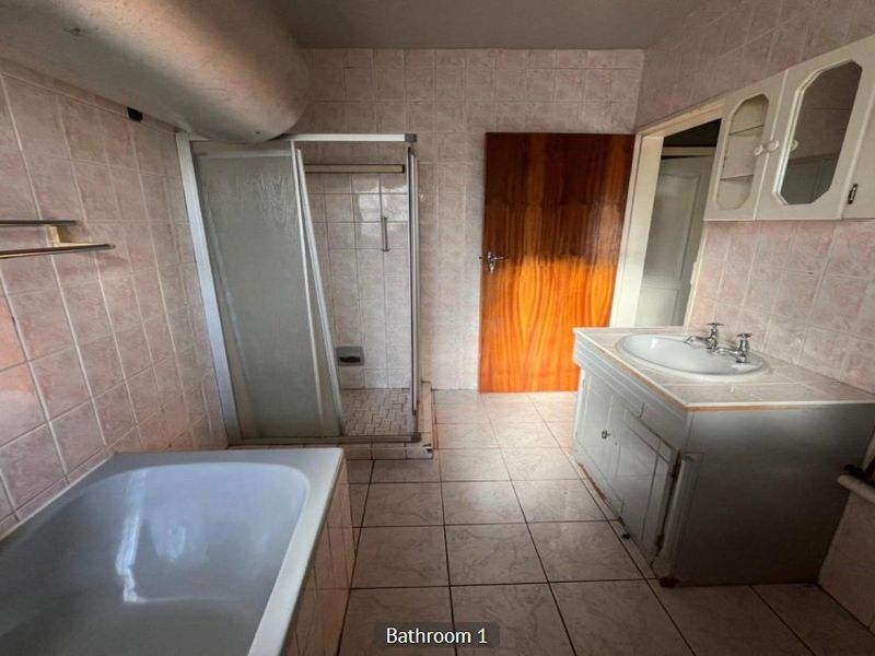 A dated bathroom featuring a shower enclosure, bathtub, and vanity cabinet with tiled walls and flooring, offering potential for a modern renovation.