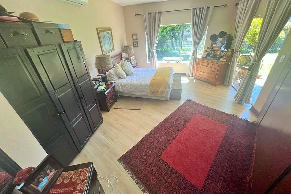 A spacious bedroom featuring light-toned laminate flooring, a split-system air conditioner, and direct access to an outdoor area through sliding glass doors.
