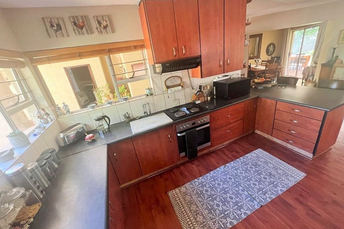A functional kitchen featuring timber cabinetry, dark laminate countertops, built-in oven, electric cooktop, and a tiled backsplash with timber flooring throughout.
