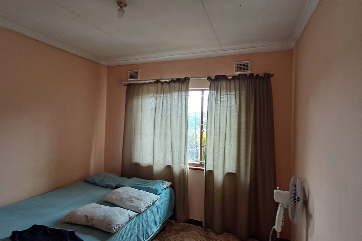 A simple bedroom featuring a window with curtain rod and ventilation grilles, requiring cosmetic updates to the walls and ceiling.