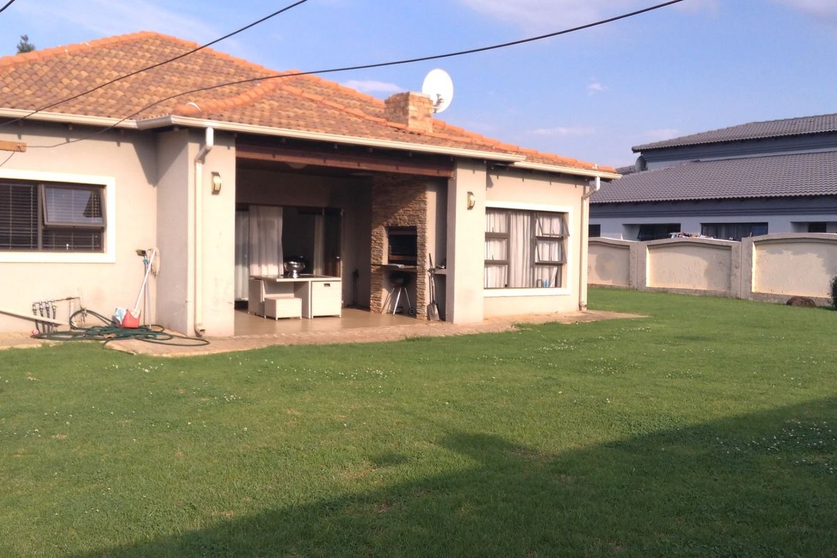 Rear view of the property featuring a covered patio with a built-in braai, tiled roof, and a spacious private garden with boundary walling.