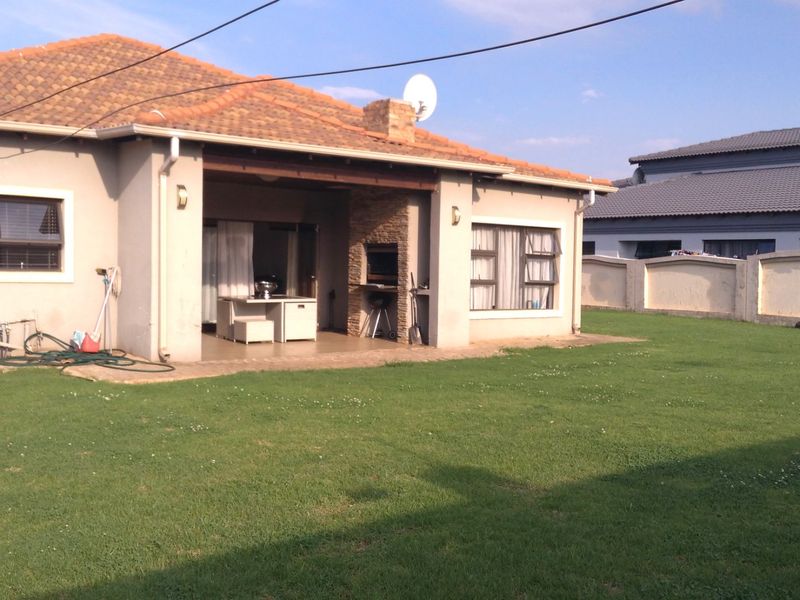 Rear view of the property featuring a covered patio with a built-in braai, tiled roof, and a spacious private garden with boundary walling.