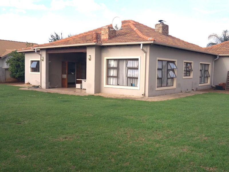 Rear view of a single-story house featuring a tiled roof, covered patio area, and a spacious lawn.