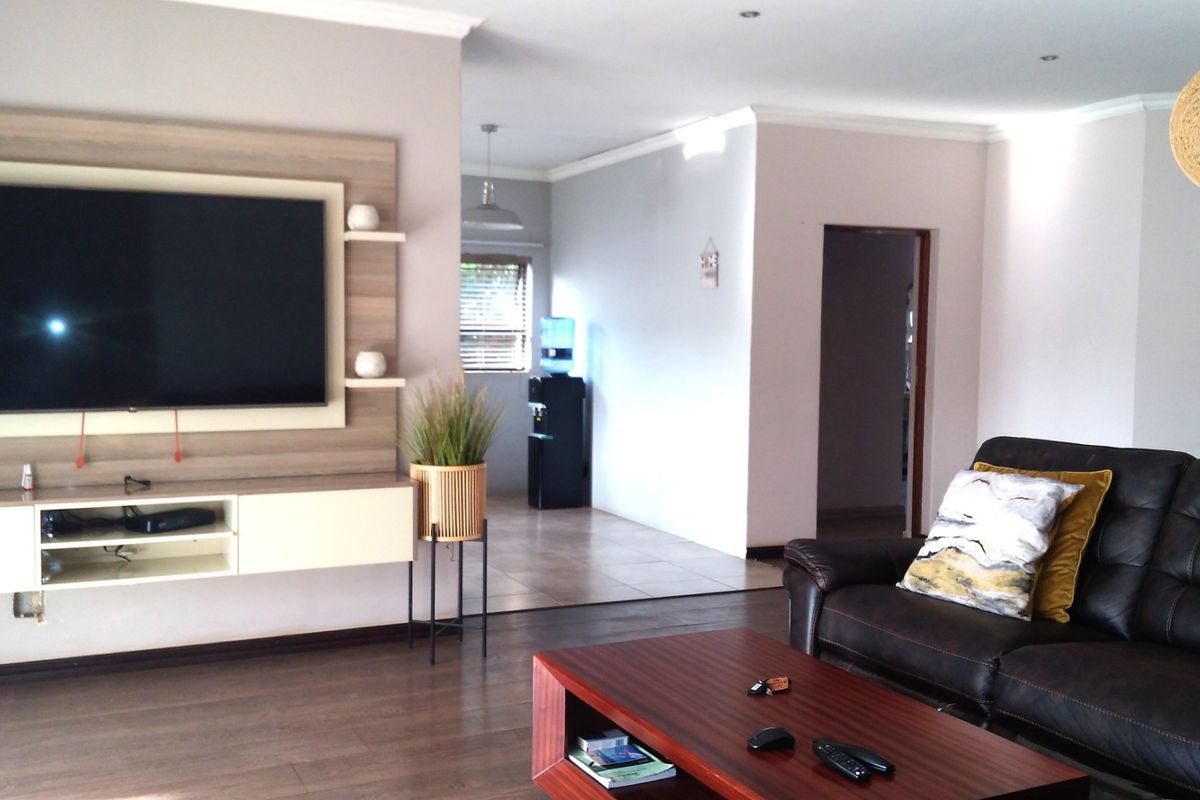 A well-maintained living room featuring a built-in media unit, recessed downlighting, and laminate flooring, leading into an adjacent hallway area.