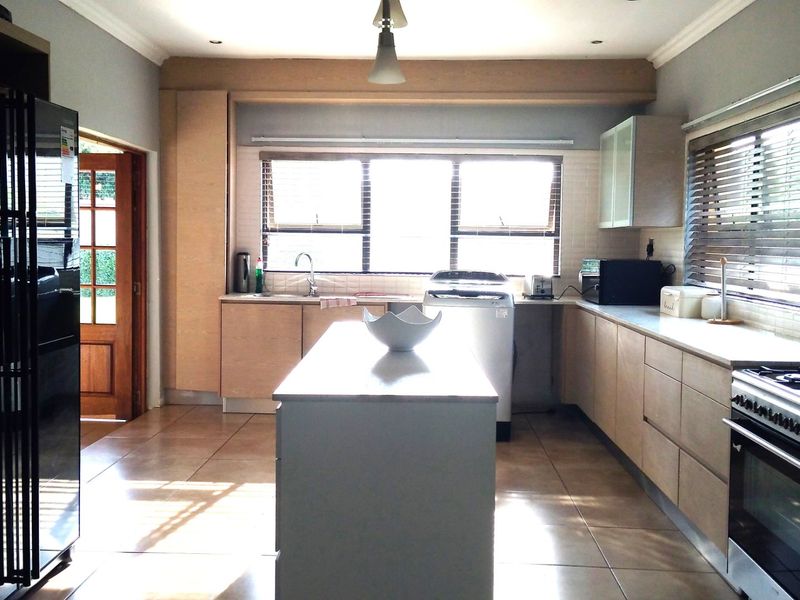 A functional kitchen featuring a central island, gas stove, built-in cabinetry, and tiled flooring with ample natural light from large windows.