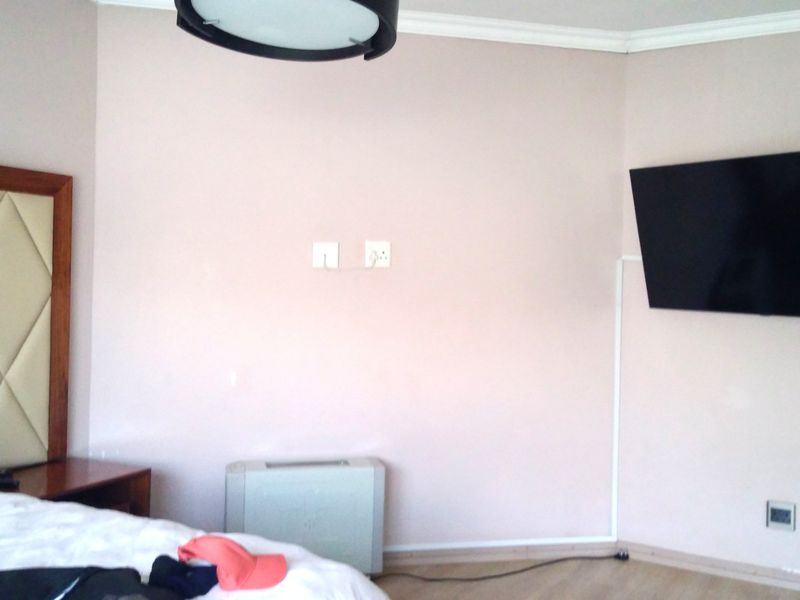 A bedroom featuring laminate flooring, coving, and a wall-mounted television with visible cable trunking.