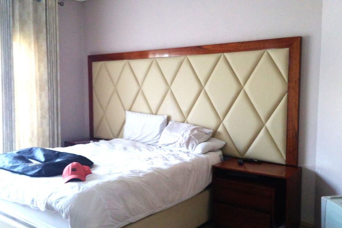 A bedroom featuring a large, custom-designed diamond-patterned upholstered headboard with integrated wooden bedside tables.