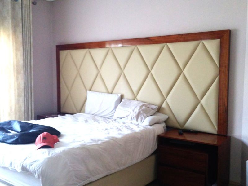 A bedroom featuring a large, custom-designed diamond-patterned upholstered headboard with integrated wooden bedside tables.