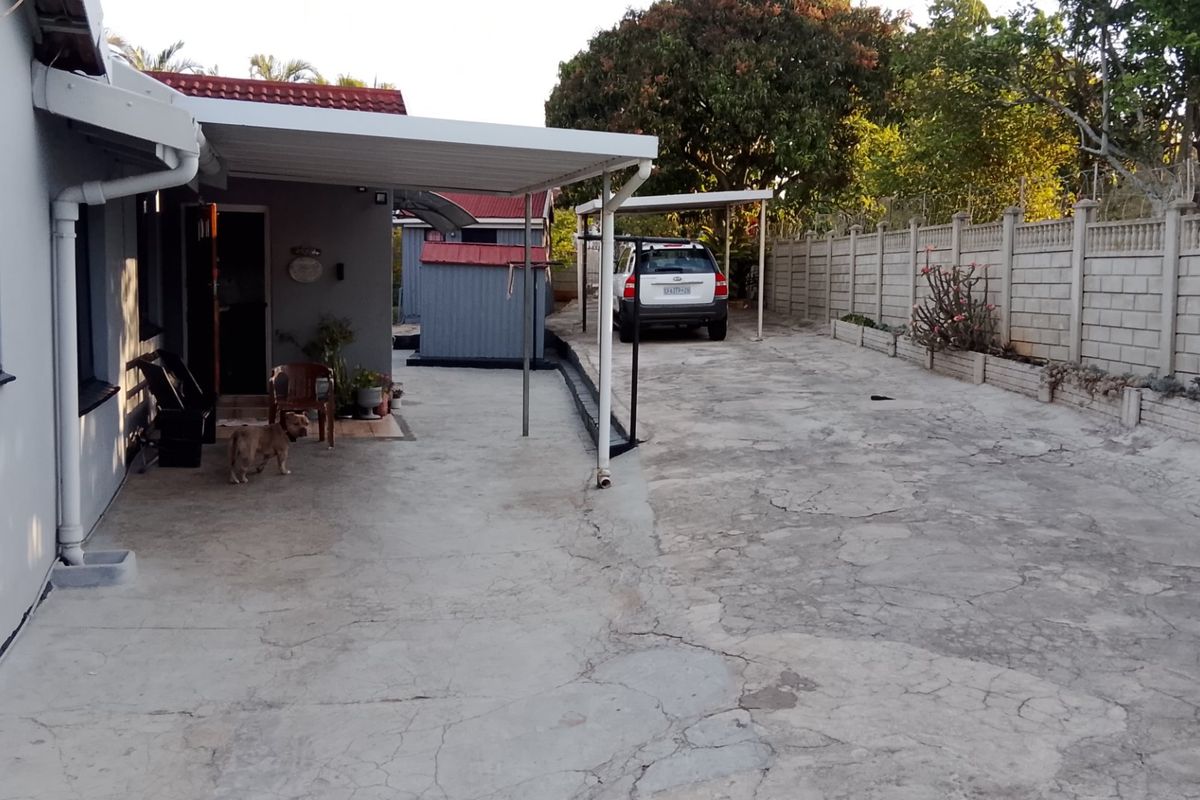 Rear exterior area featuring a concrete driveway, carport structure, and precast concrete boundary walling.