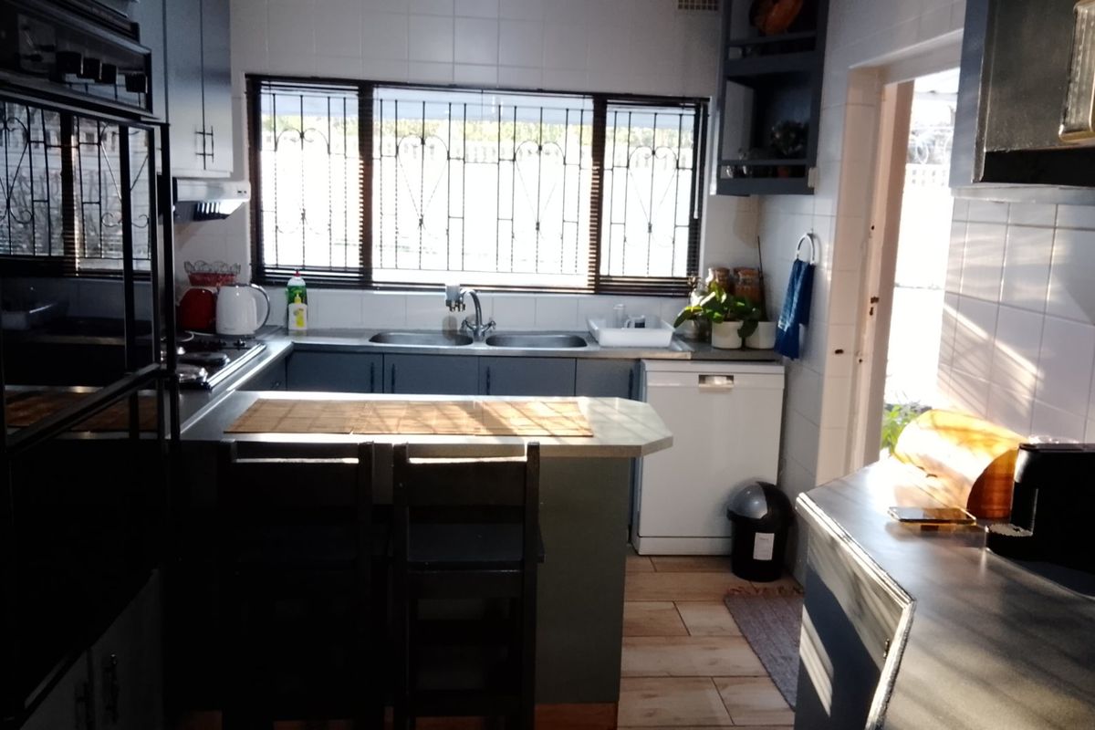 Functional kitchen featuring built-in oven, extractor fan, double sink, tiled splashback, and ample cabinetry with a breakfast counter layout.