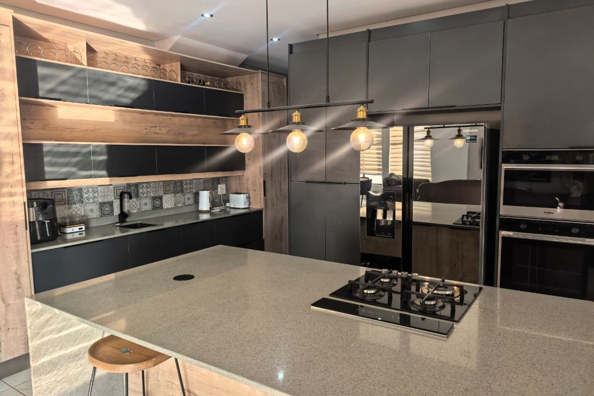 Modern kitchen featuring a large island with gas cooktop, stone countertops, integrated cabinetry, built-in appliances, and stylish pendant lighting.