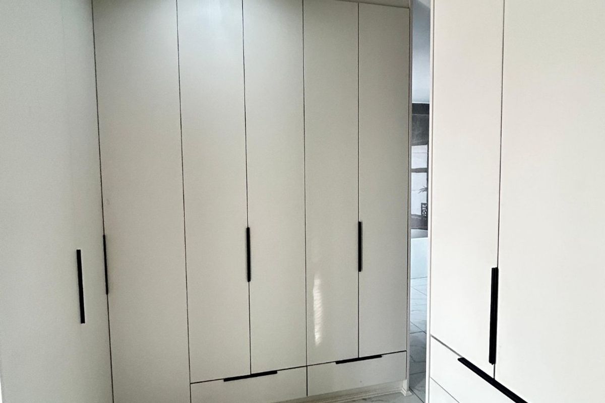 A modern, minimalist dressing area or bedroom featuring extensive floor-to-ceiling built-in cabinetry with sleek black handles and polished marble-look tiled flooring.