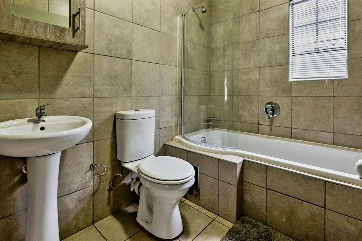 A functional bathroom featuring a pedestal basin, toilet, and a bathtub with a glass shower screen, finished with neutral wall and floor tiles.