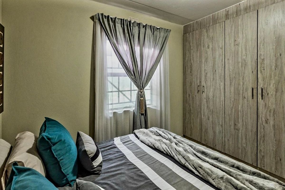 A well-maintained bedroom featuring floor-to-ceiling wood-finish built-in cupboards and a window fitted with security bars.