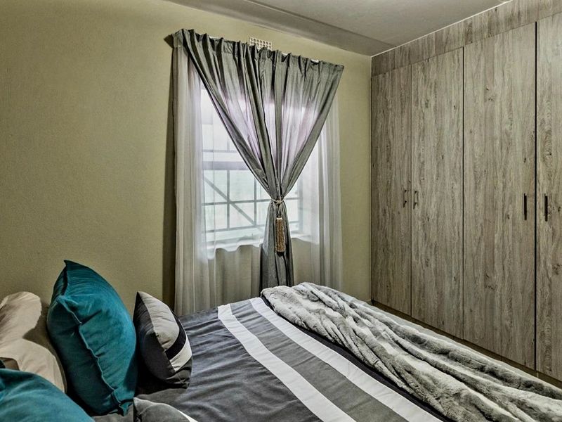 A well-maintained bedroom featuring floor-to-ceiling wood-finish built-in cupboards and a window fitted with security bars.