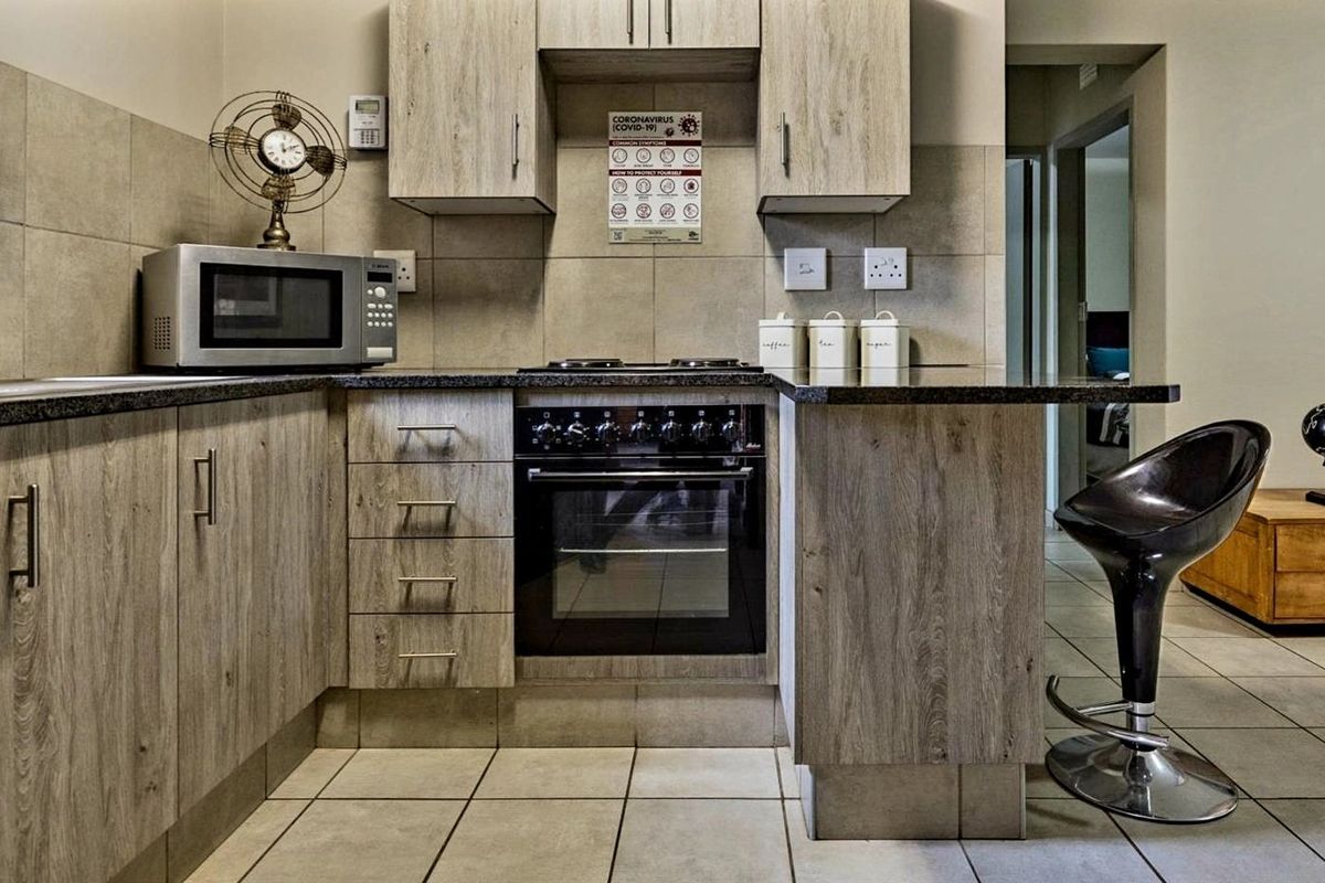 A functional kitchen featuring wood-look cabinetry, granite countertops, a built-in oven and hob, and neutral tiled flooring.