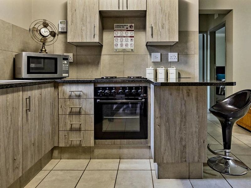 A functional kitchen featuring wood-look cabinetry, granite countertops, a built-in oven and hob, and neutral tiled flooring.