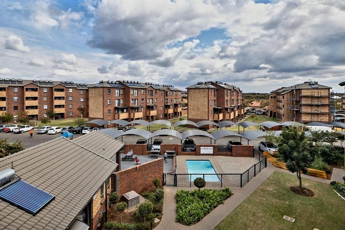Aerial view of an apartment complex featuring a communal swimming pool, covered parking bays, and well-maintained landscaped grounds.