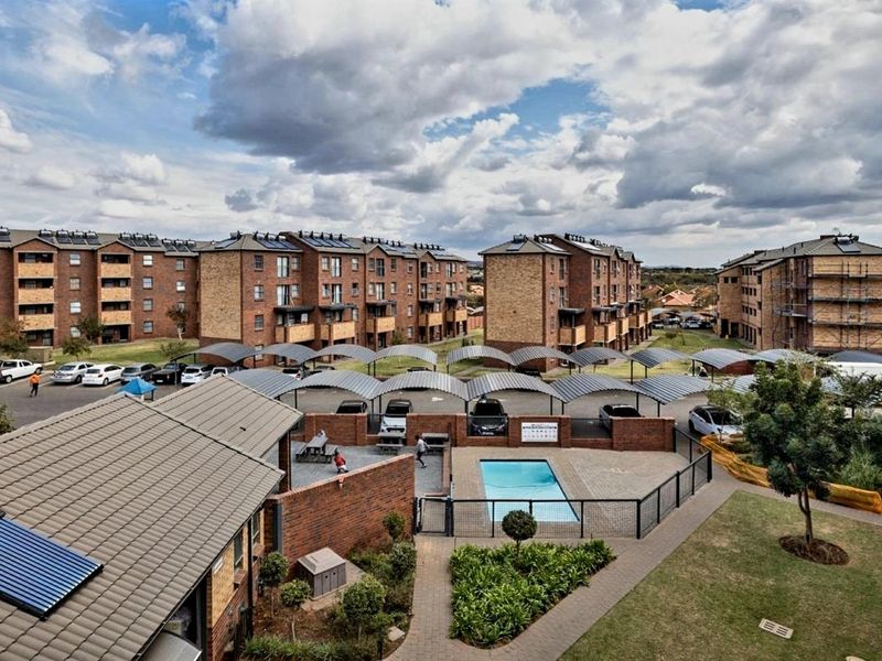 Aerial view of an apartment complex featuring a communal swimming pool, covered parking bays, and well-maintained landscaped grounds.