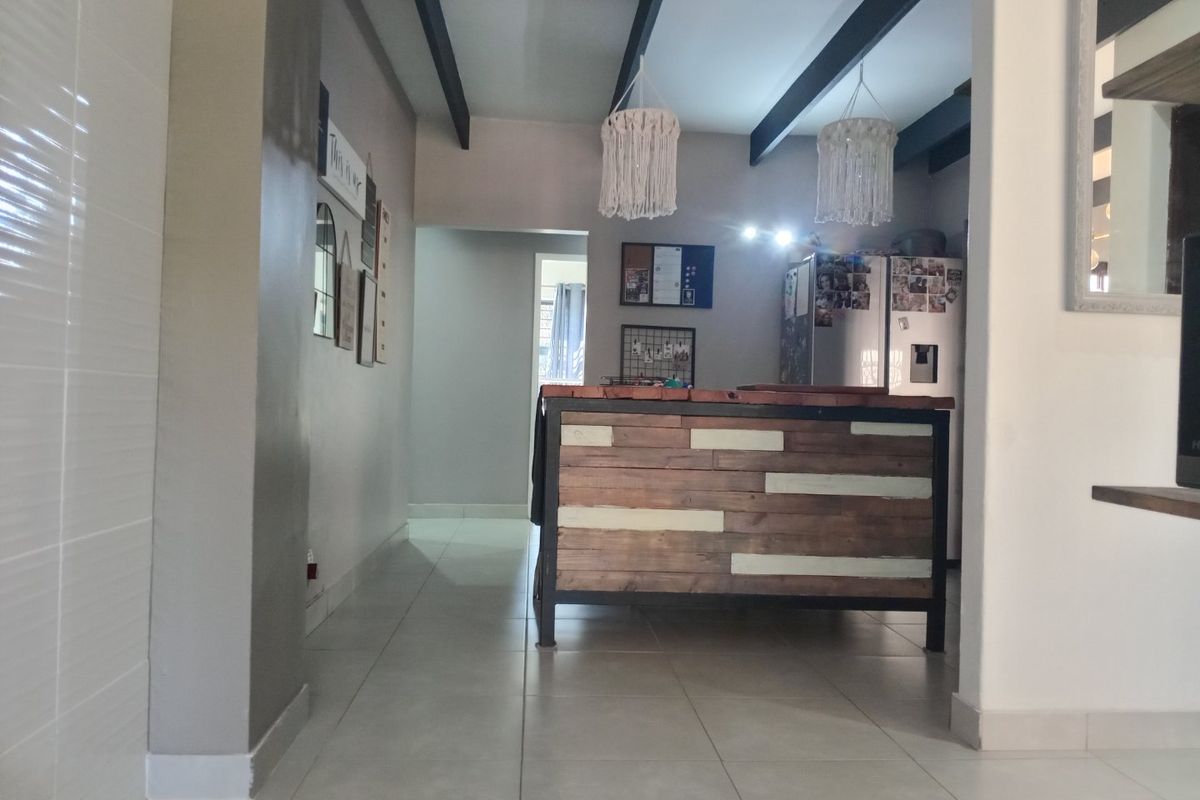 A kitchen area featuring a rustic timber-clad island, exposed ceiling beams, and neutral tiled flooring, offering a functional layout with modern design elements.