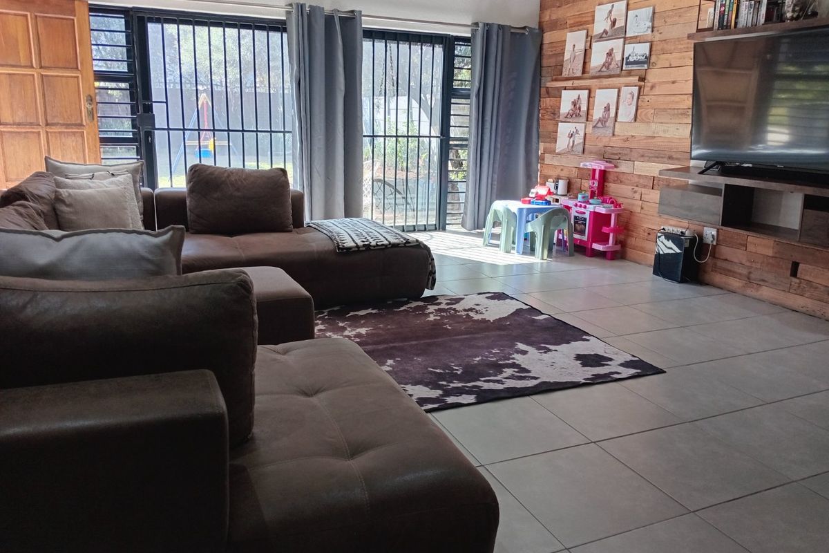 Spacious living room featuring large format floor tiles, a rustic timber feature wall, and sliding doors with security gates leading to the garden.