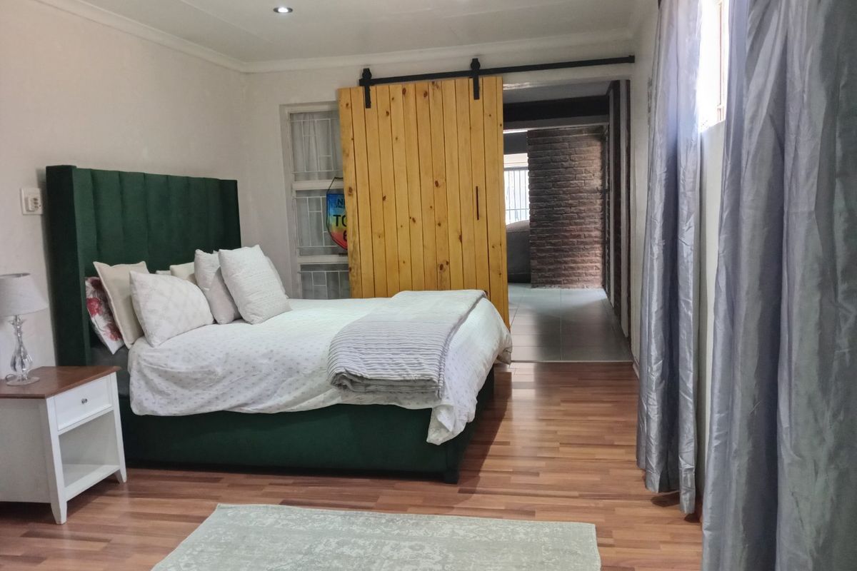 A well-maintained bedroom featuring laminate flooring, recessed downlighting, and a distinctive wooden sliding barn door leading to an adjacent space.