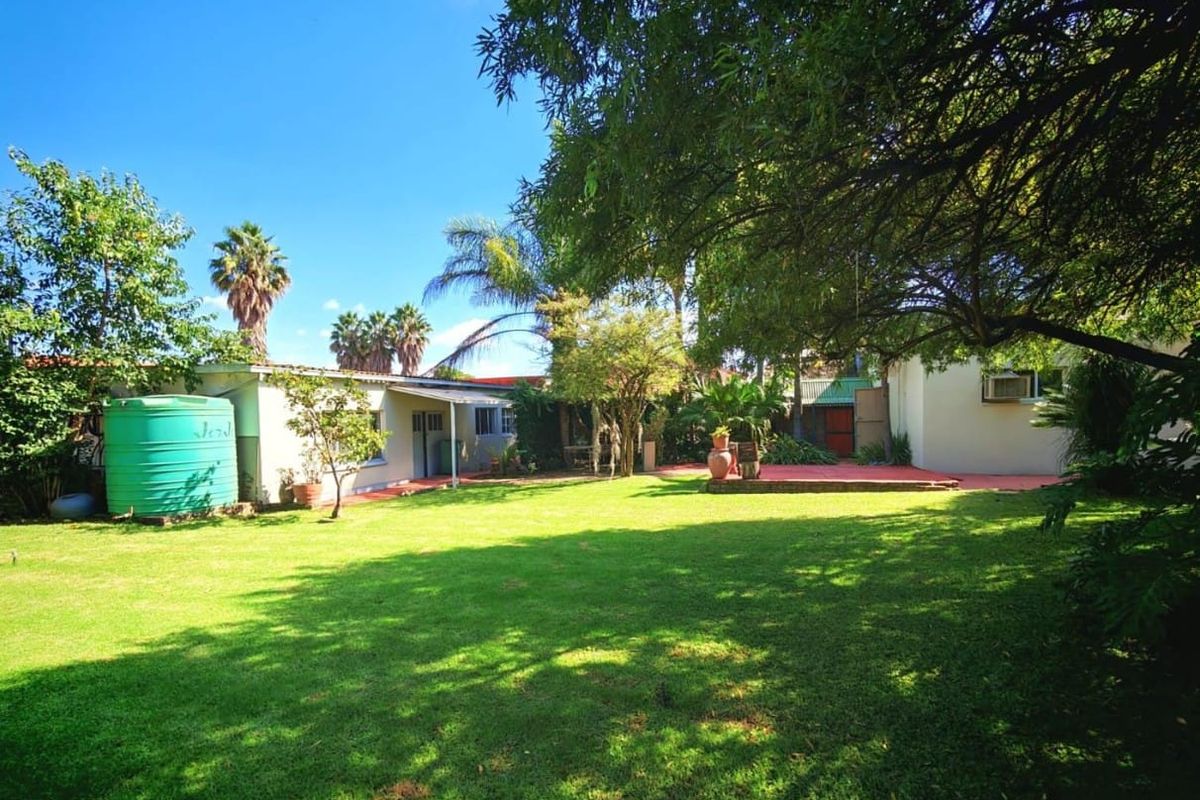 A spacious rear garden featuring a well-maintained lawn, mature trees, a paved patio area, and an external water storage tank.