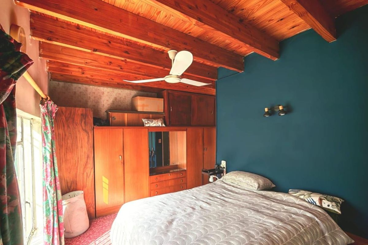 A bedroom featuring exposed timber ceiling beams, built-in wooden cabinetry, and a ceiling fan, finished with a bold accent wall.