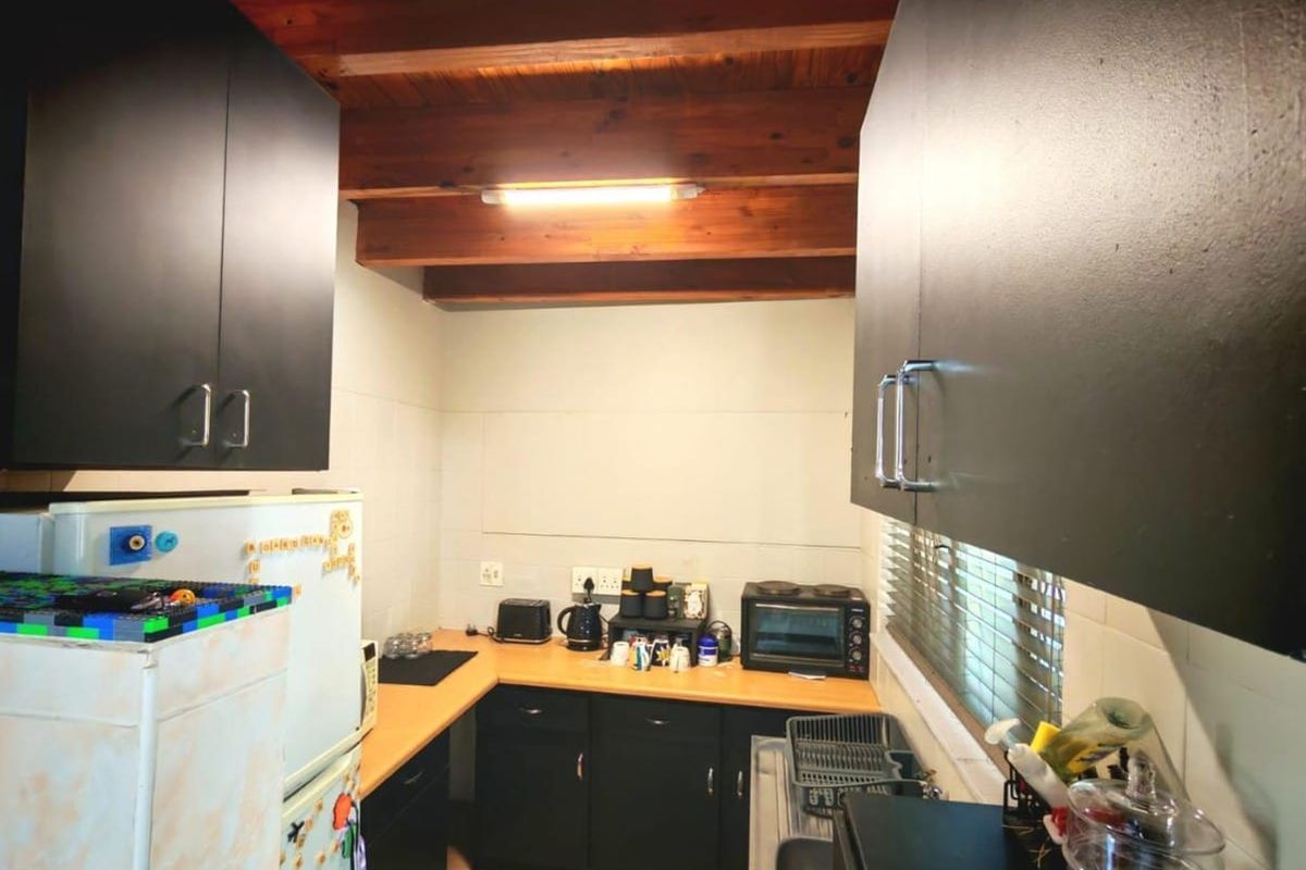 Compact kitchen featuring dark cabinetry, laminate countertops, tiled splashbacks, and exposed timber ceiling beams.