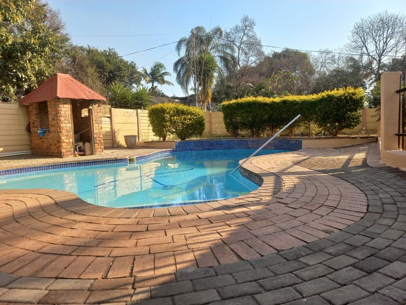 Outdoor pool area featuring a swimming pool with brick paving, a small brick gazebo, and established garden hedging.