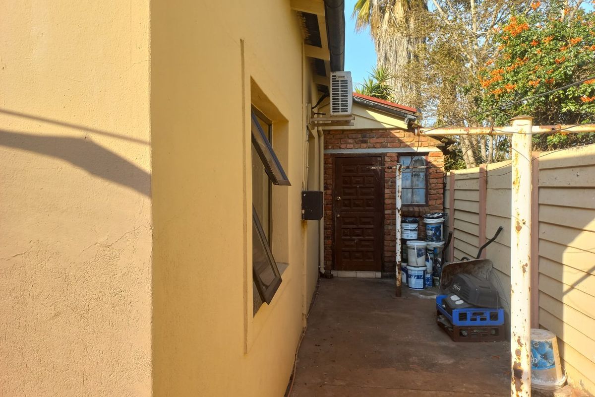 A side exterior view of the property showing a paved walkway, air conditioning unit, and boundary wall.