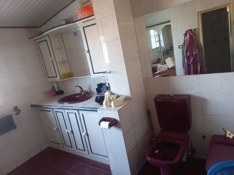 A dated bathroom featuring burgundy sanitaryware, tiled surfaces, and built-in vanity cabinetry, offering significant potential for a modern renovation.