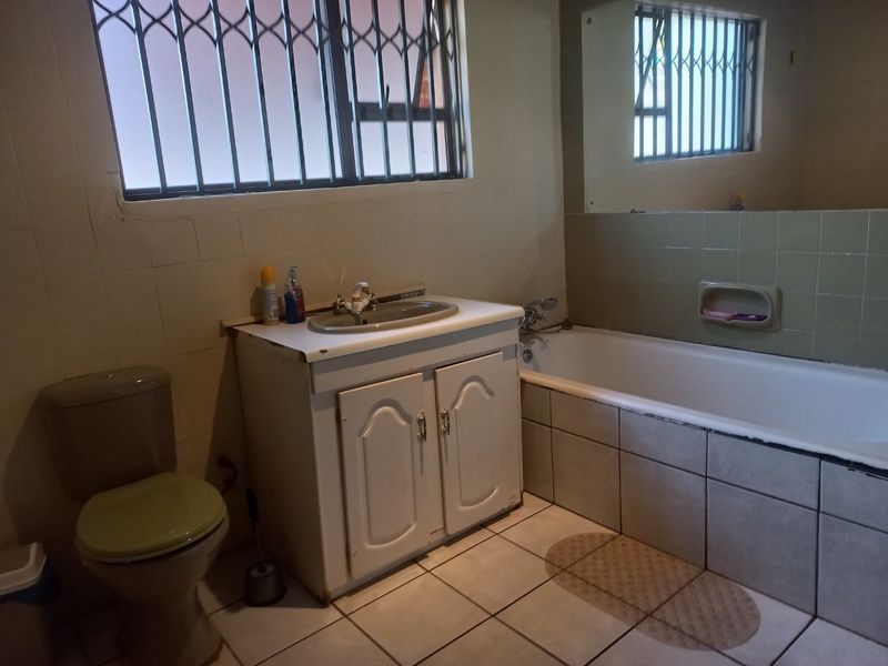 A dated bathroom featuring a built-in vanity, bathtub, and tiled finishes, equipped with security bars on the window.