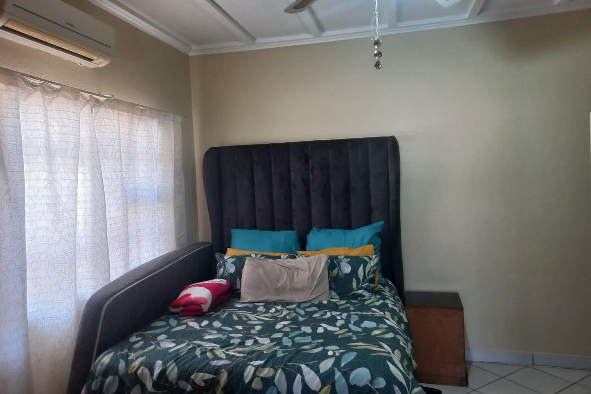 A bedroom featuring tiled flooring, a ceiling fan, and a wall-mounted split-system air conditioning unit.